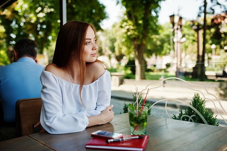 Portrait of a beautiful businesswoman sitting at a table with red notebook, pen, smartphone and a drink on it.