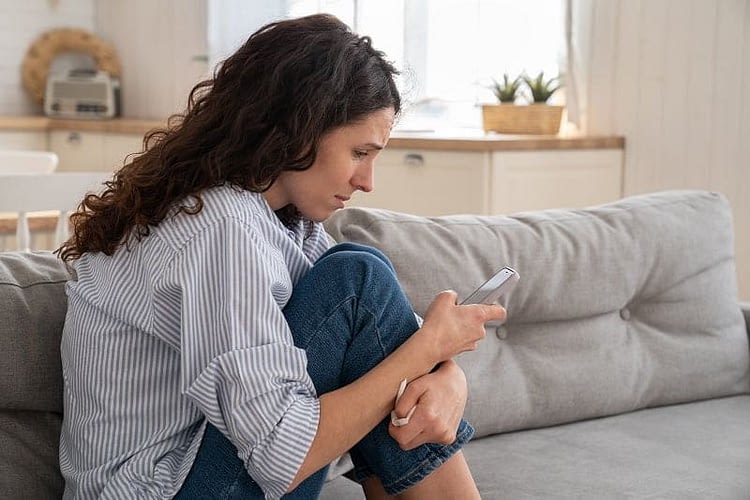 desperate and sad sitting woman on couch holding a phone texting